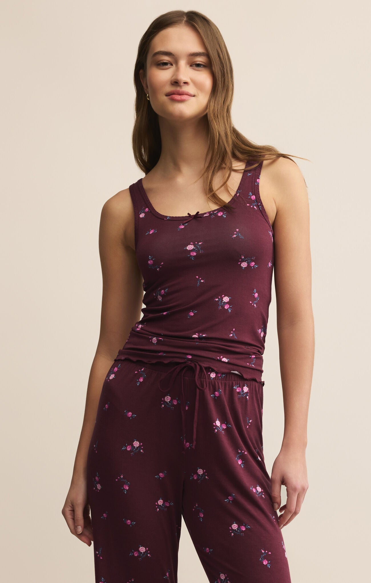 Woman wearing a maroon sleeveless top and pants with floral pattern on a beige background
