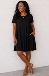 Woman wearing a black dress standing against a white brick wall.