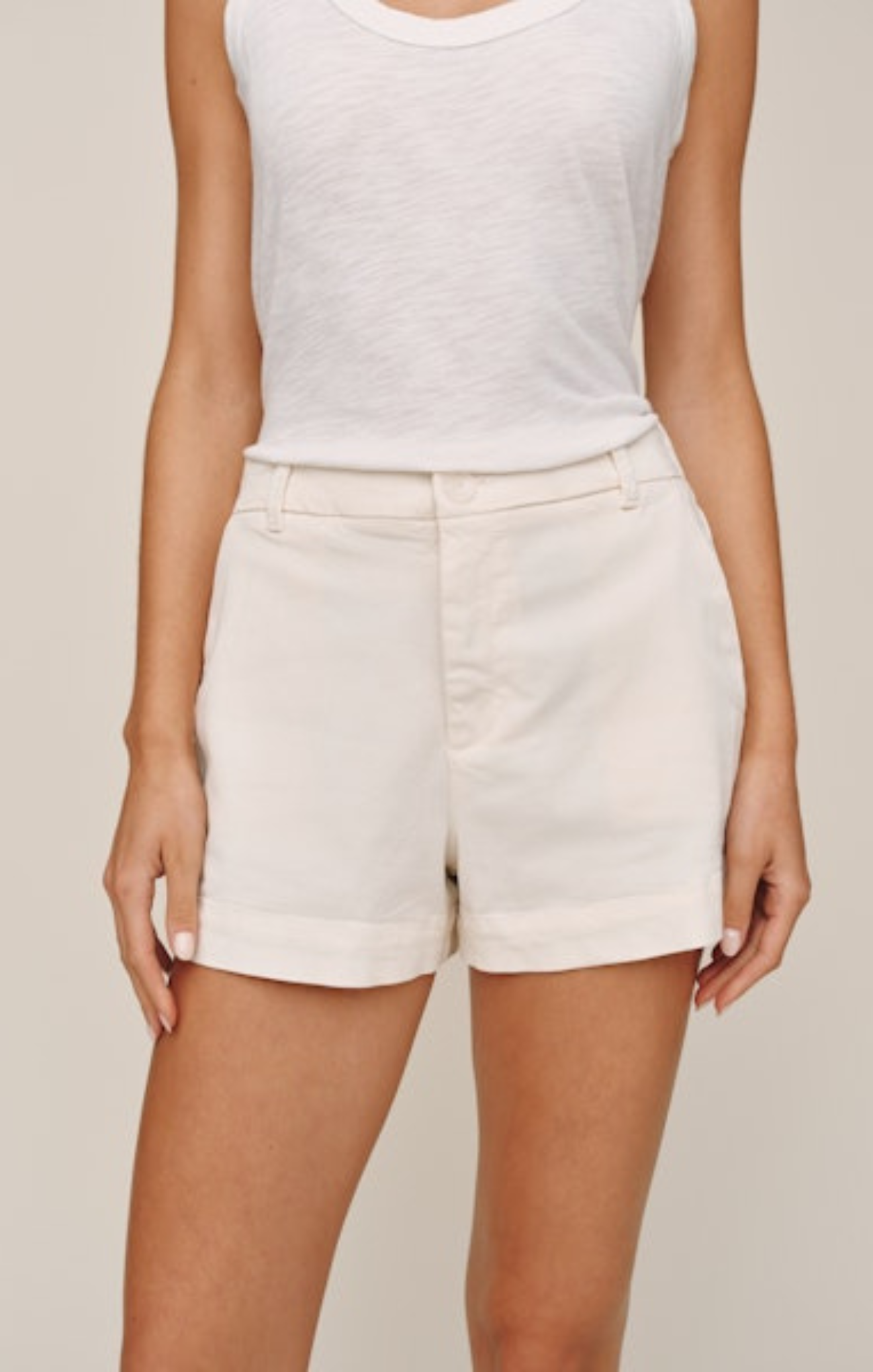 Person wearing a white tank top and beige shorts on a plain background
