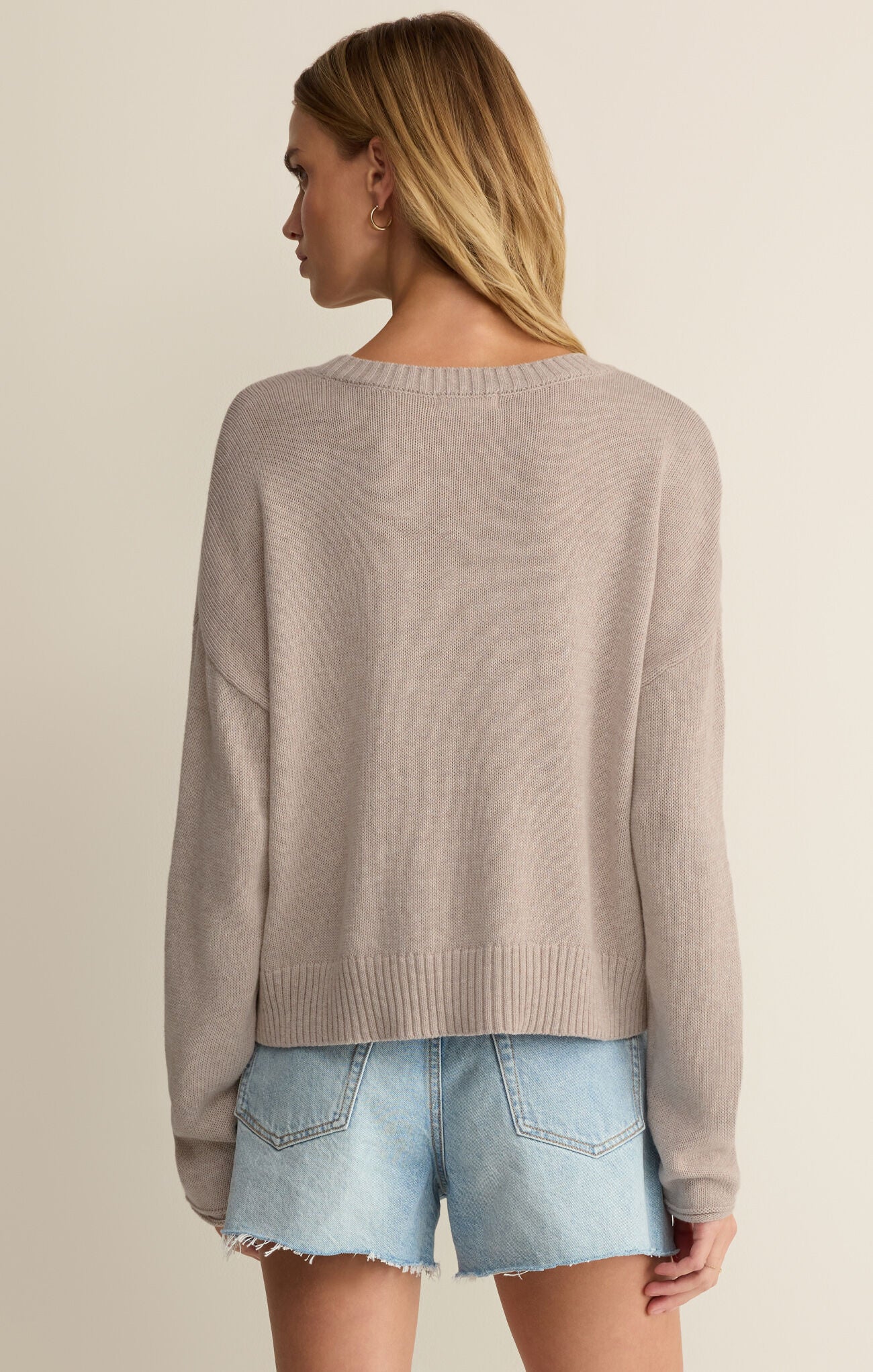 Woman wearing a beige sweater and denim shorts on a plain background