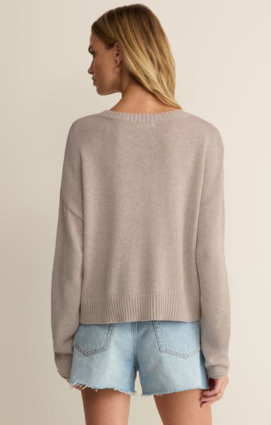 Woman wearing a beige sweater and denim shorts on a plain background