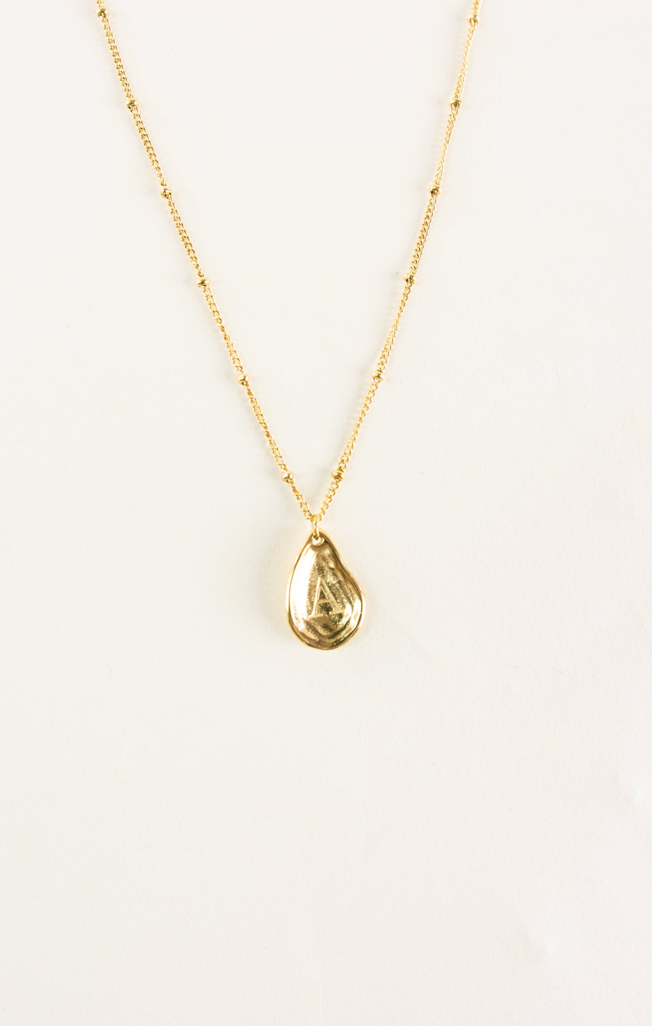 Gold necklace with a teardrop pendant on a light beige background