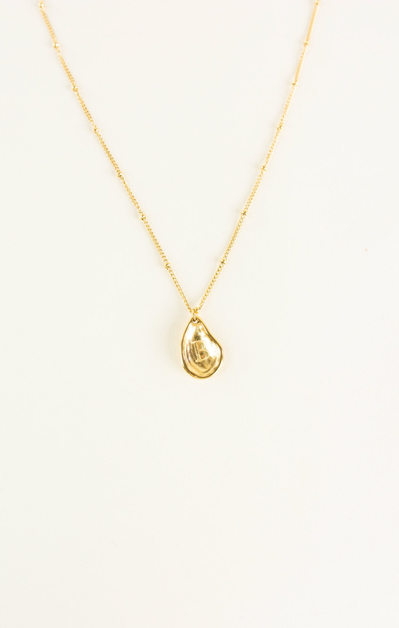 Gold necklace with a teardrop pendant on a white background