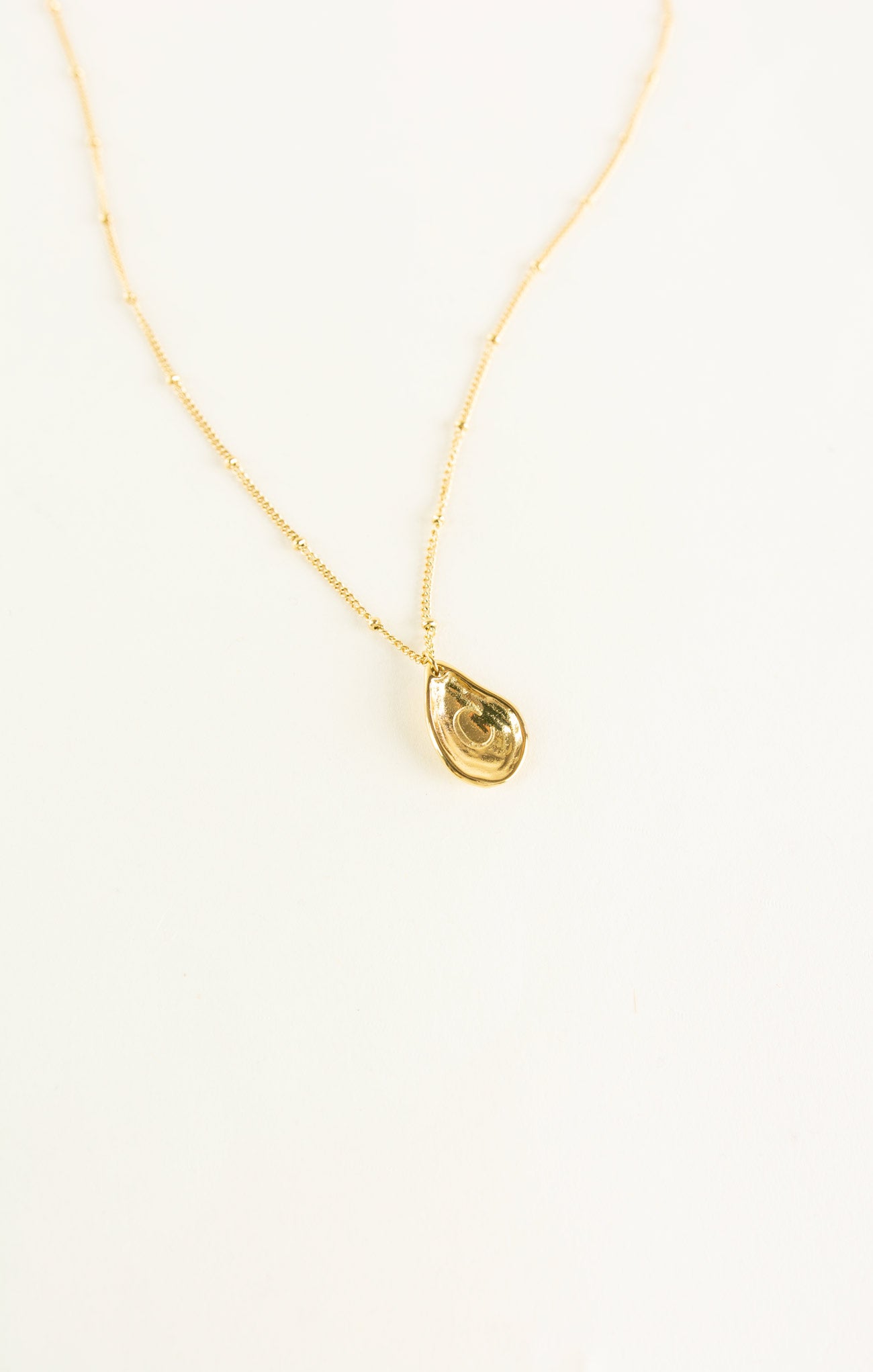 Gold necklace with a teardrop-shaped pendant on a white background