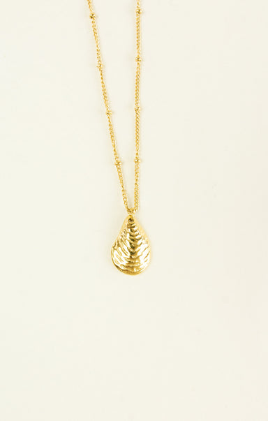 Gold necklace with a teardrop pendant on a beige background