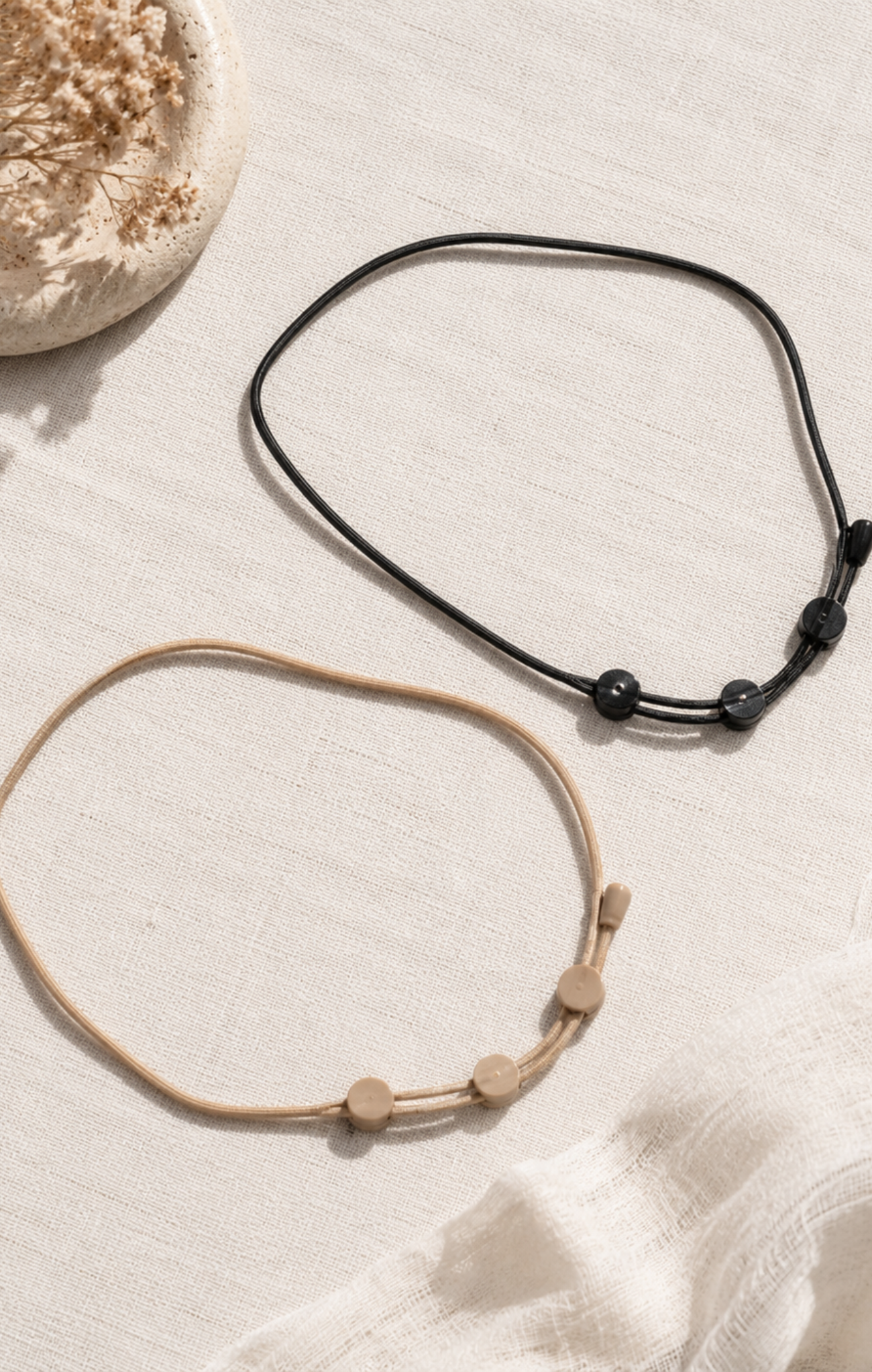 Two necklaces, one black and one beige with small beads, on a light textured surface.