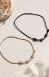 Two necklaces, one black and one beige with small beads, on a light textured surface.
