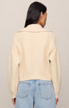 Person wearing a beige ribbed sweater and blue jeans against a neutral background