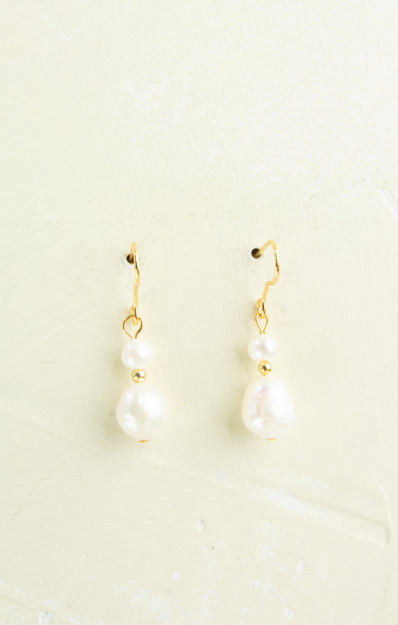 Pair of pearl earrings with gold hooks on a light beige background