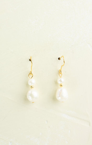 Pair of pearl earrings with gold hooks on a light beige background