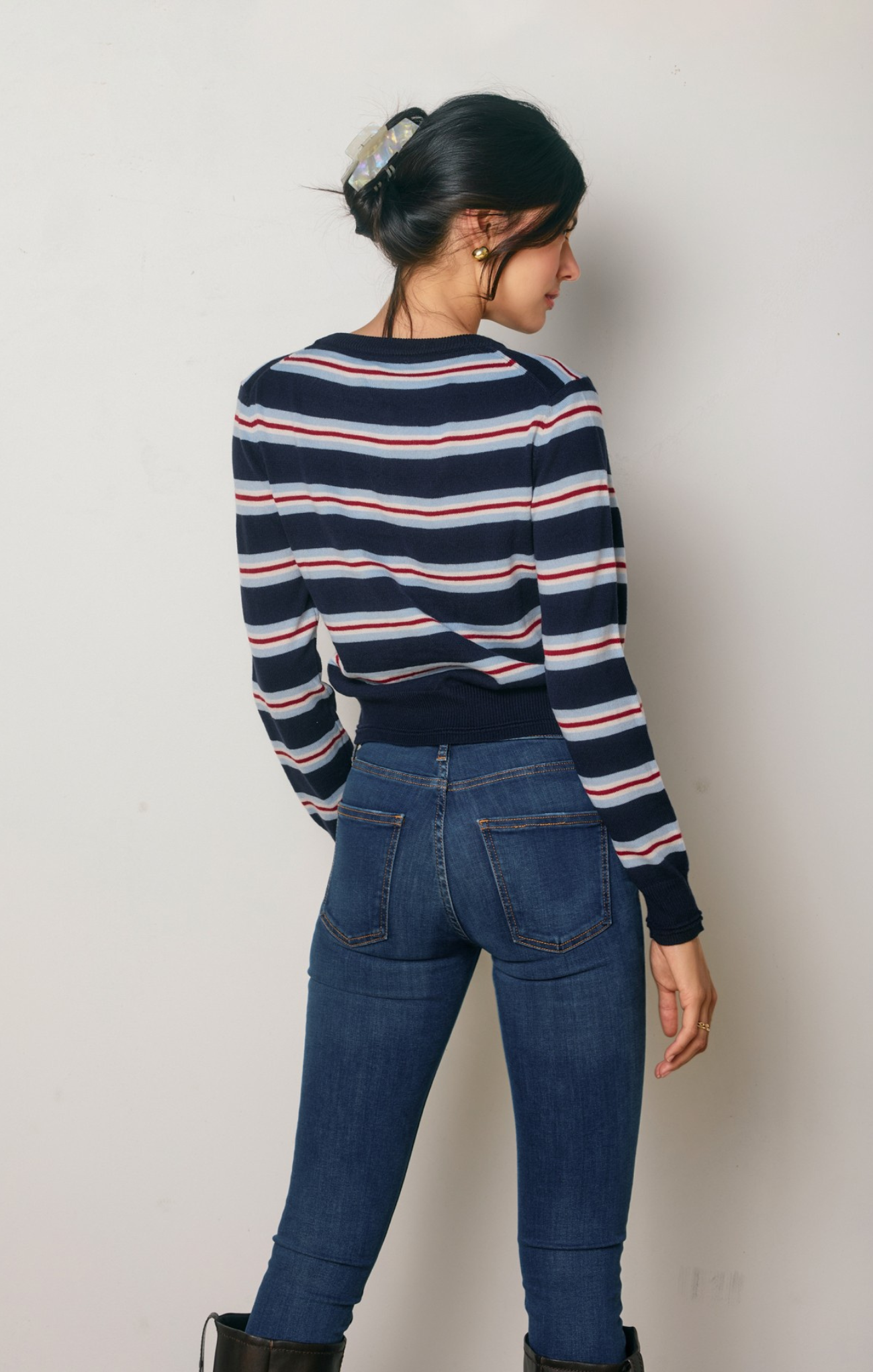 Person wearing a striped sweater and blue jeans against a plain background