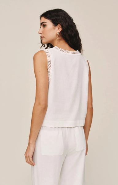 Woman wearing a white sleeveless top with intricate detailing on a beige background