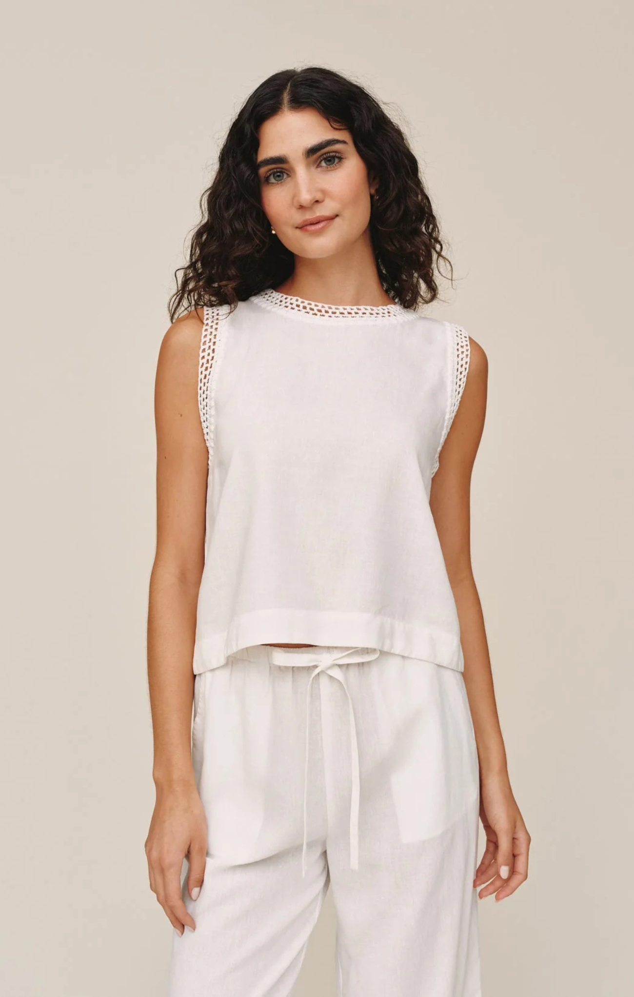 Woman wearing a white sleeveless top and pants against a beige background