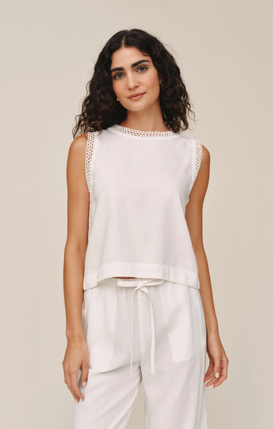 Woman wearing a white sleeveless top and pants against a beige background