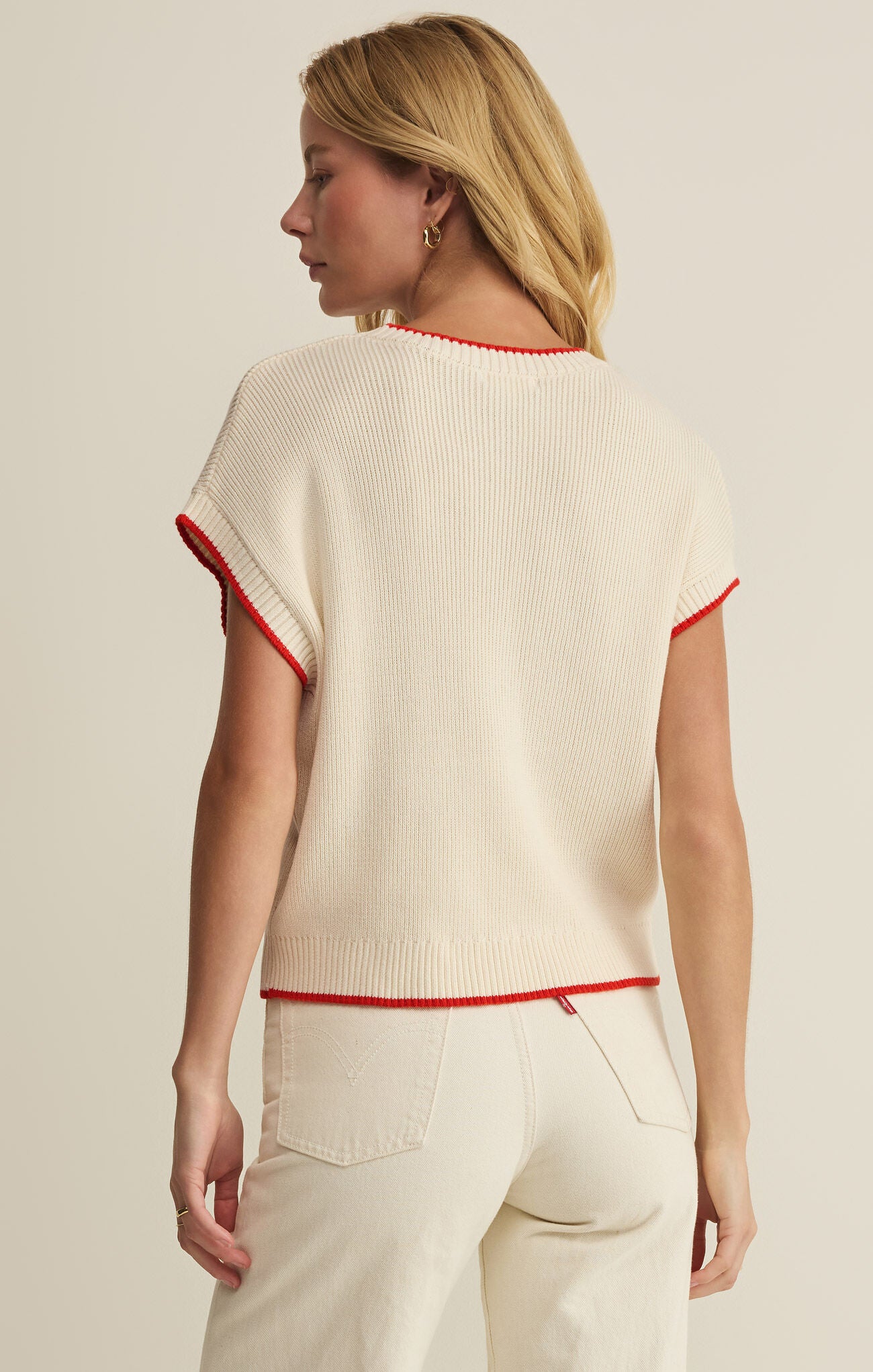 Woman wearing a cream sweater with red trim on a beige background
