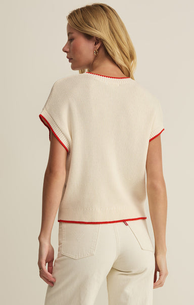 Woman wearing a cream sweater with red trim on a beige background