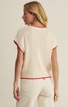 Woman wearing a cream sweater with red trim on a beige background