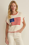 Woman wearing a cream-colored sweater with an American flag design on a beige background