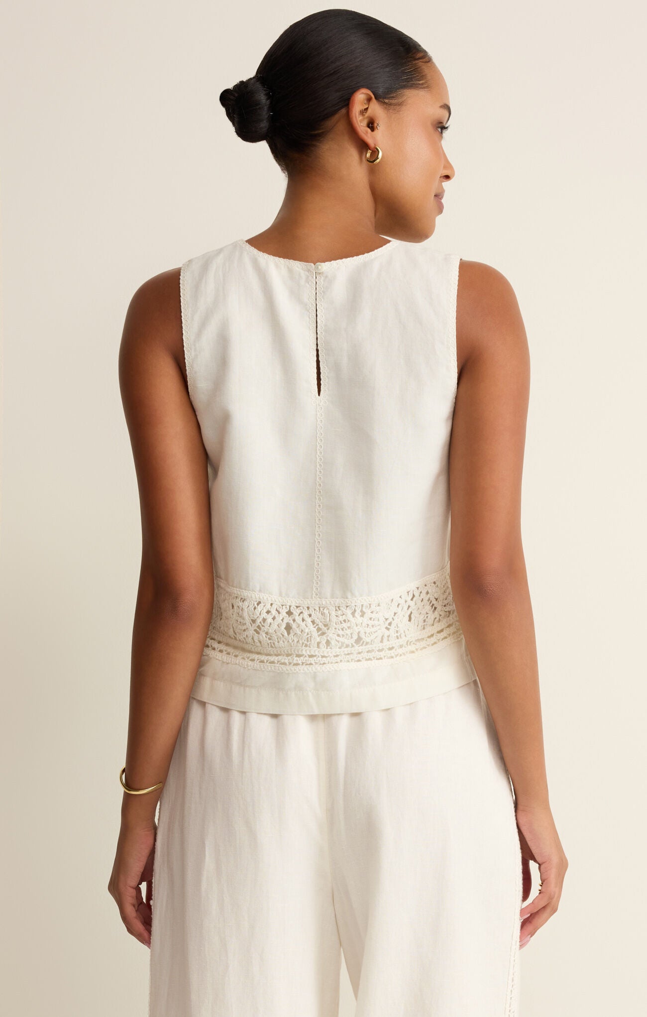 Woman wearing a white sleeveless dress with lace details on a beige background