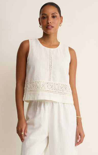 Woman wearing a sleeveless white top with lace details on a beige background