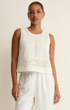 Woman wearing a sleeveless white top with lace details on a beige background