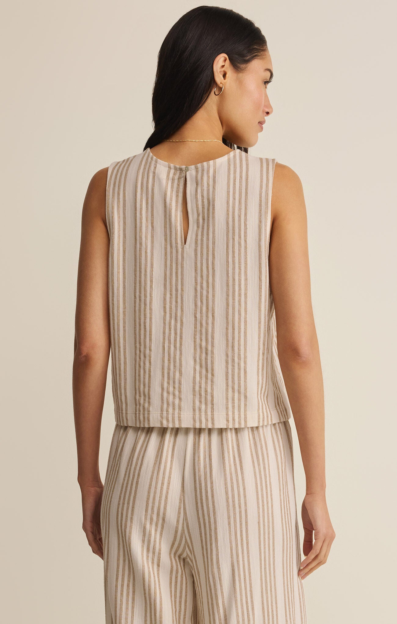 Woman wearing a beige and white striped sleeveless top and pants on a plain background