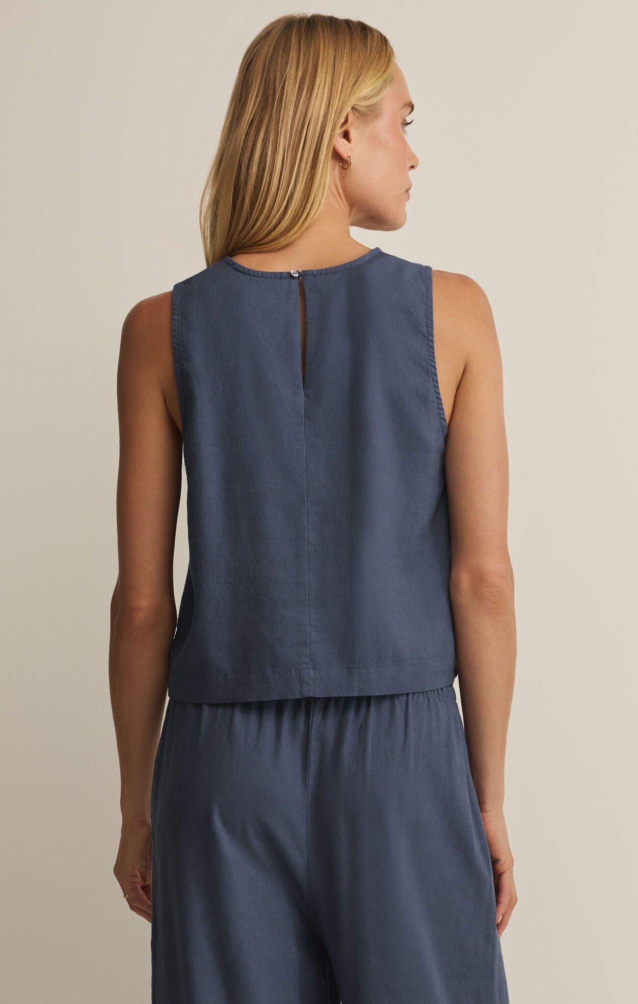 Woman wearing a sleeveless blue top and matching pants on a beige background