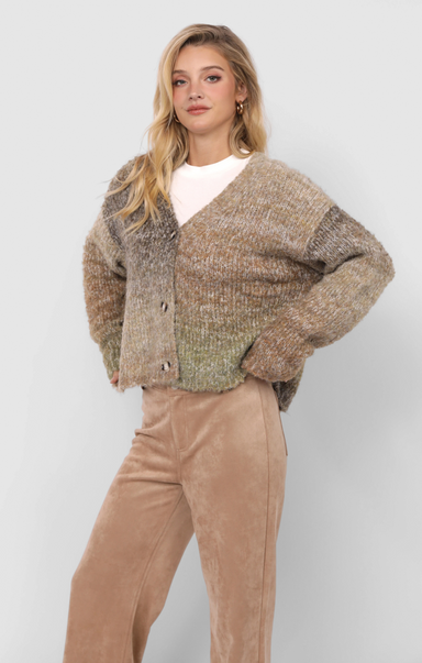 Woman wearing a patterned cardigan and beige pants against a white background