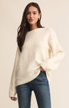 Woman wearing a cream sweater and blue jeans against a beige background