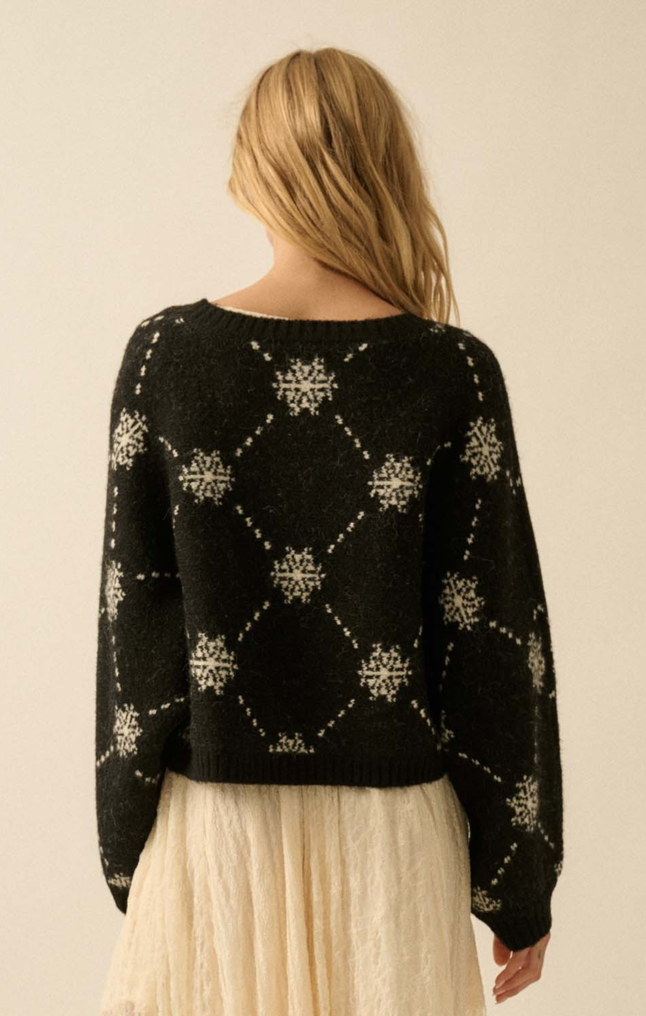 Person wearing a black sweater with white patterns on a beige background