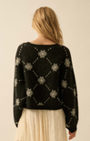 Person wearing a black sweater with white patterns on a beige background