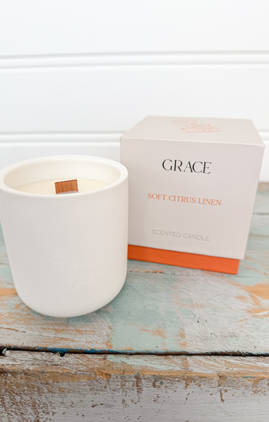 White candle with a 'Grace' box on a wooden surface