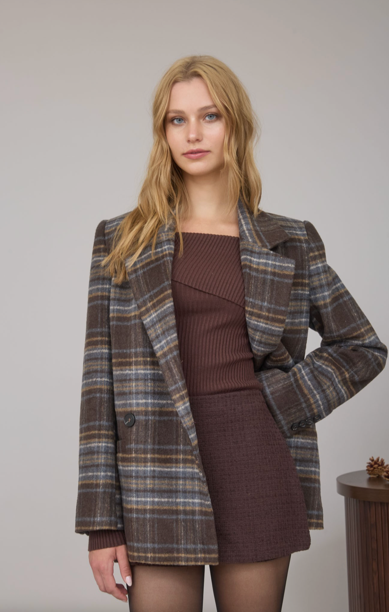 Woman wearing a plaid coat over a brown dress on a plain background