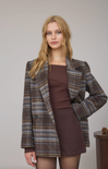 Woman wearing a plaid coat over a brown dress on a plain background