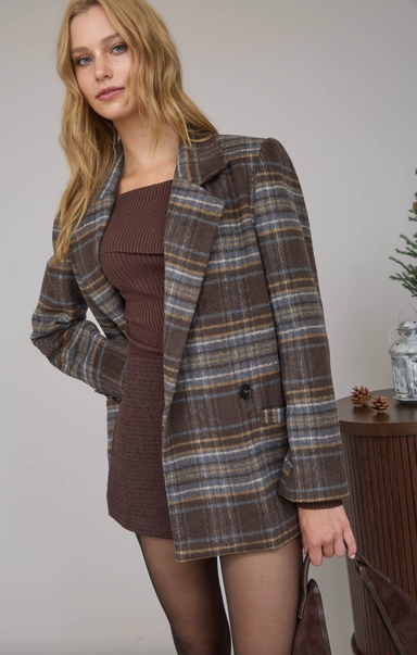 Woman wearing a plaid coat over a brown dress against a neutral background