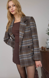 Woman wearing a plaid coat over a brown dress against a neutral background