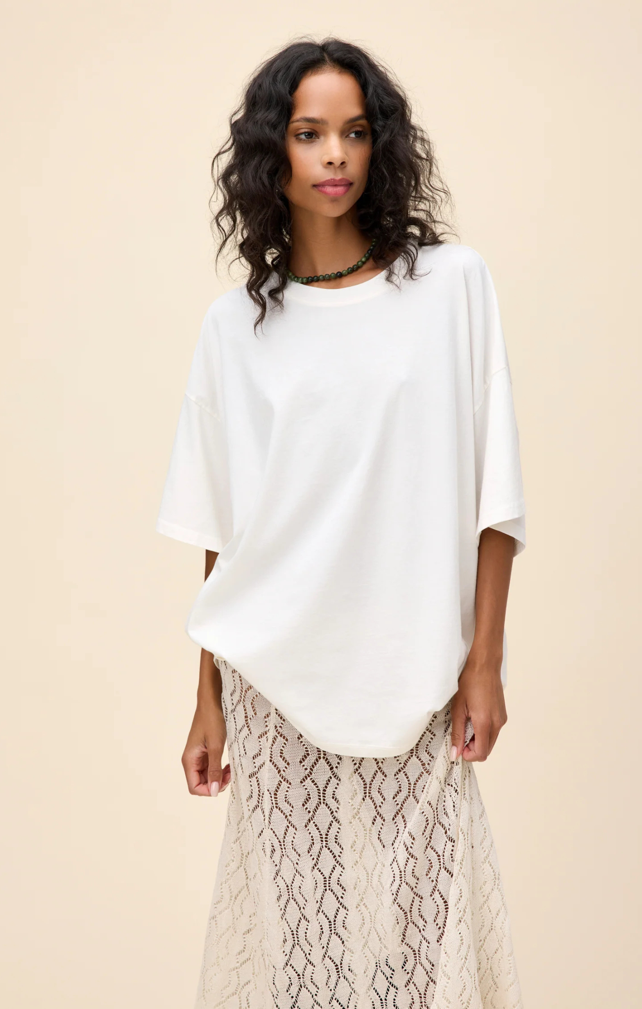 Woman wearing a white top and patterned skirt against a beige background