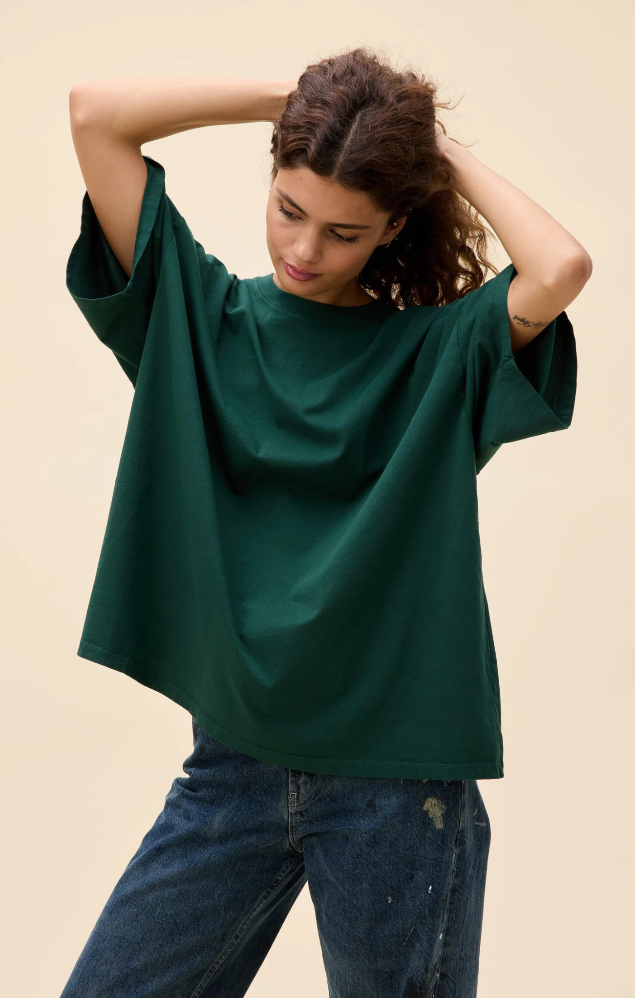 Woman wearing a green oversized top and blue jeans against a beige background