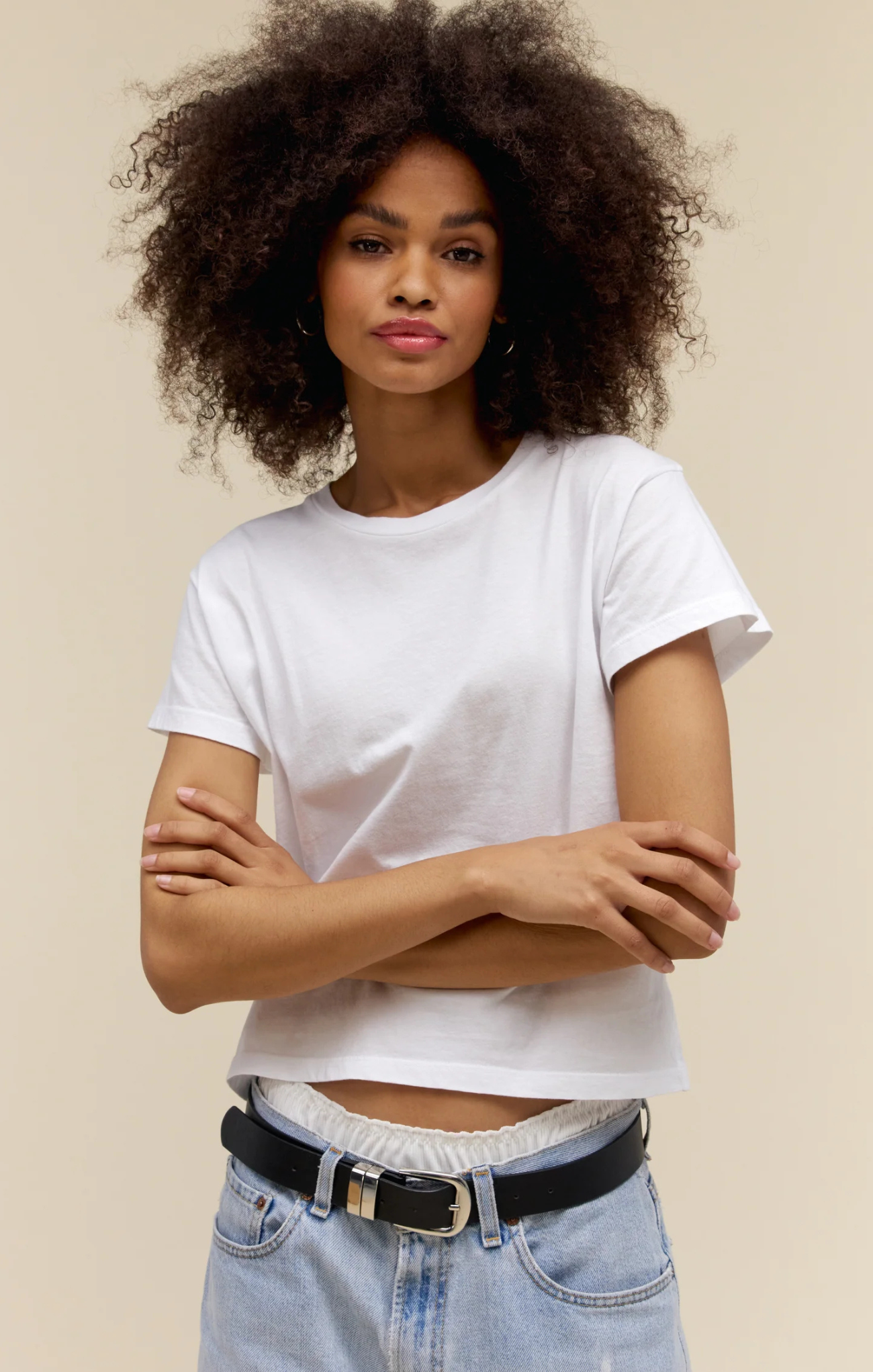 Woman wearing a white t-shirt and blue jeans with a beige background