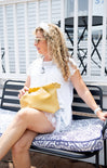 Woman sitting on a bench with a yellow bag, wearing a white outfit.