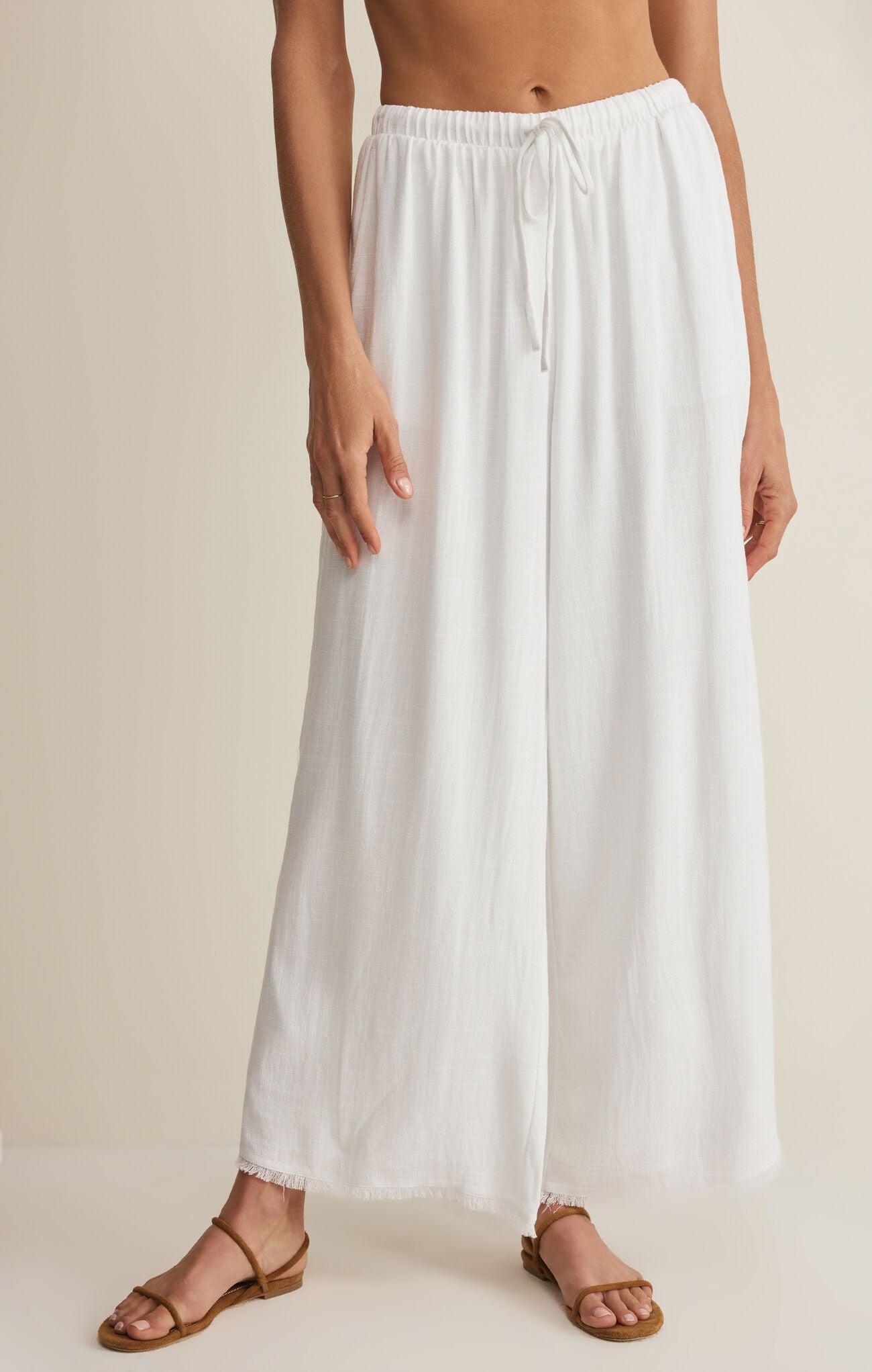 Person wearing a white wide-leg pants on a beige background
