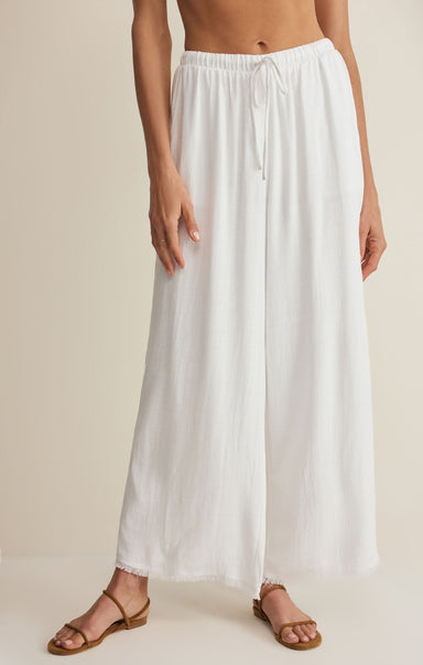 Person wearing a white wide-leg pants on a beige background