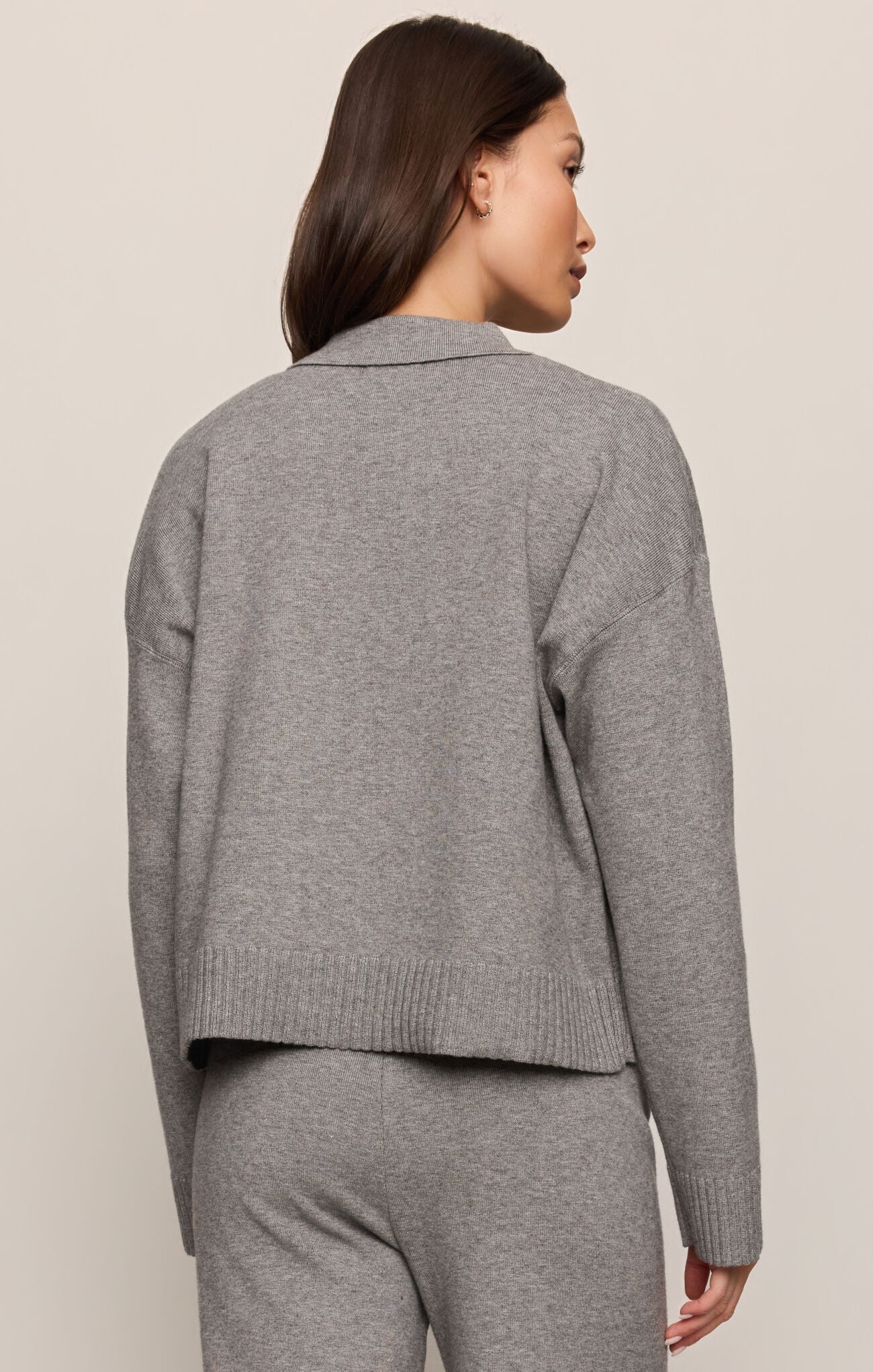 Person wearing a gray knit cardigan and pants on a beige background