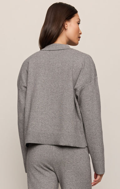 Person wearing a gray knit cardigan and pants on a beige background