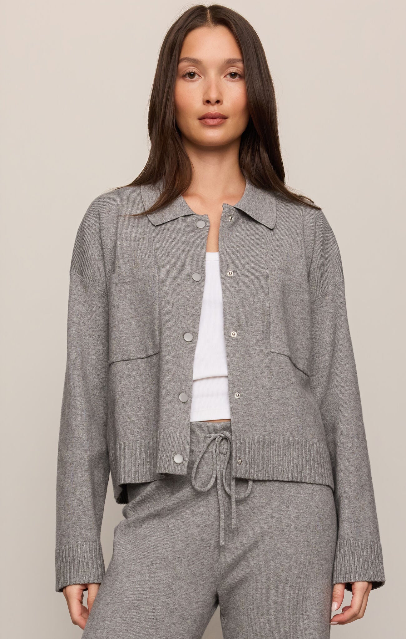 Woman wearing a gray textured jacket over a white top and gray pants on a beige background