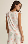 Woman wearing a white sleeveless top and pants with floral patterns on a plain background