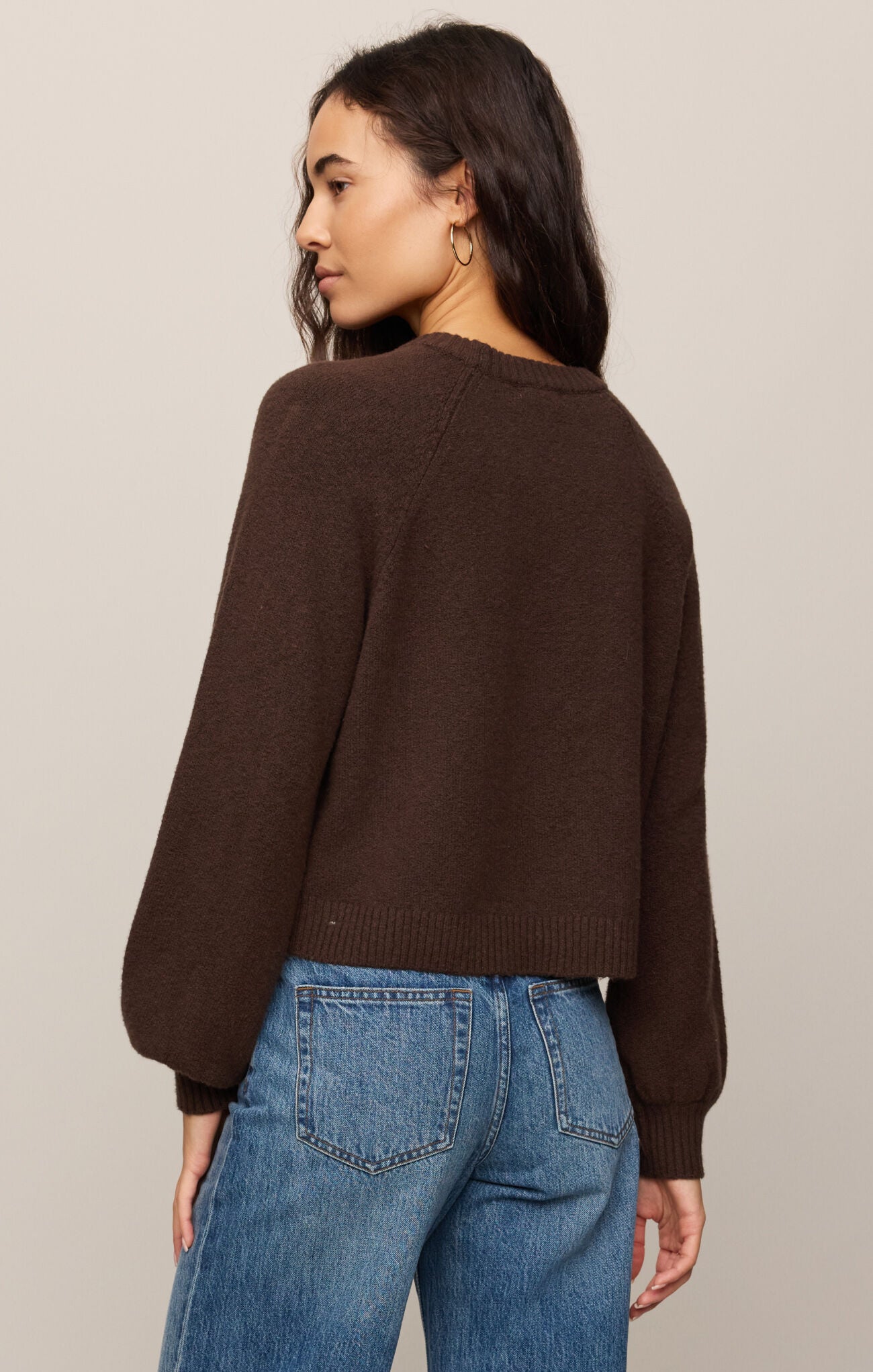 Person wearing a brown sweater and blue jeans against a neutral background