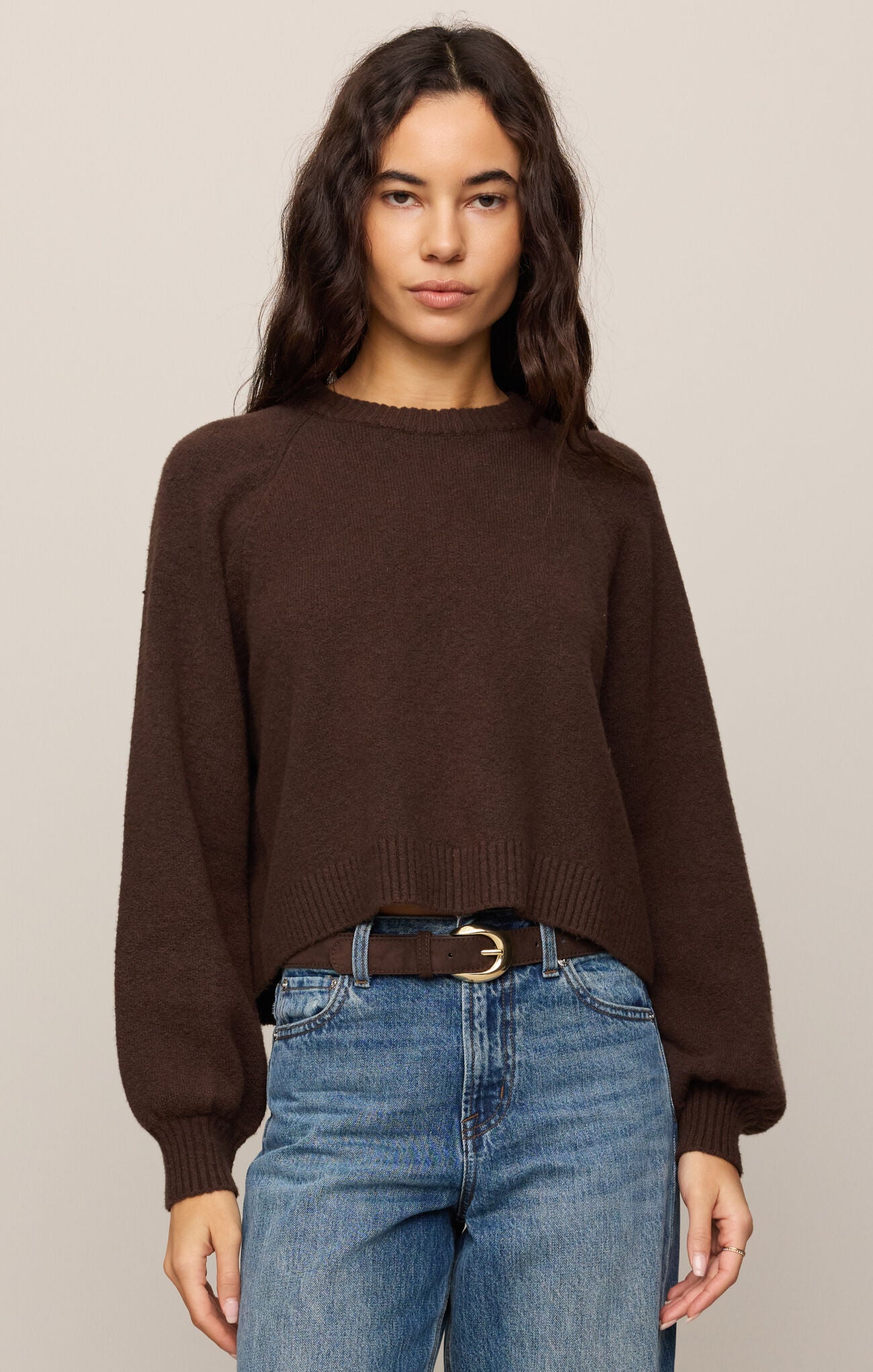 Woman wearing a brown sweater and blue jeans against a plain background