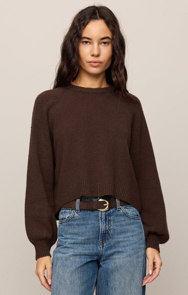 Woman wearing a brown sweater and blue jeans against a plain background