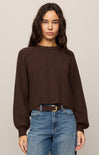 Woman wearing a brown sweater and blue jeans against a plain background